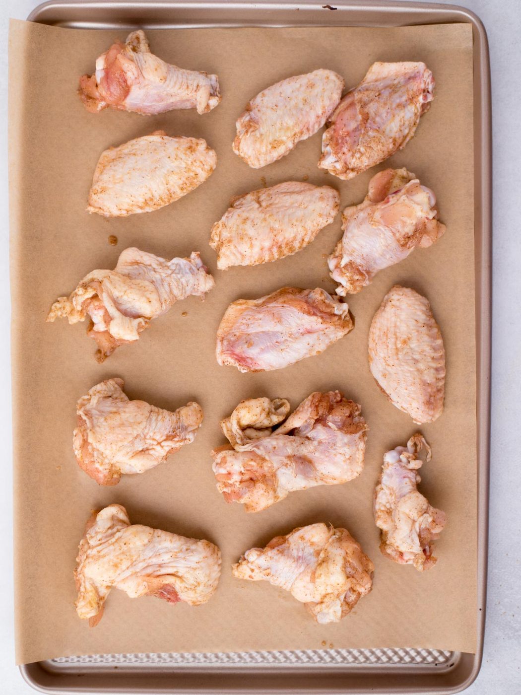 Seasoned chicken wings laying on a parchment paper covered baking sheet.
