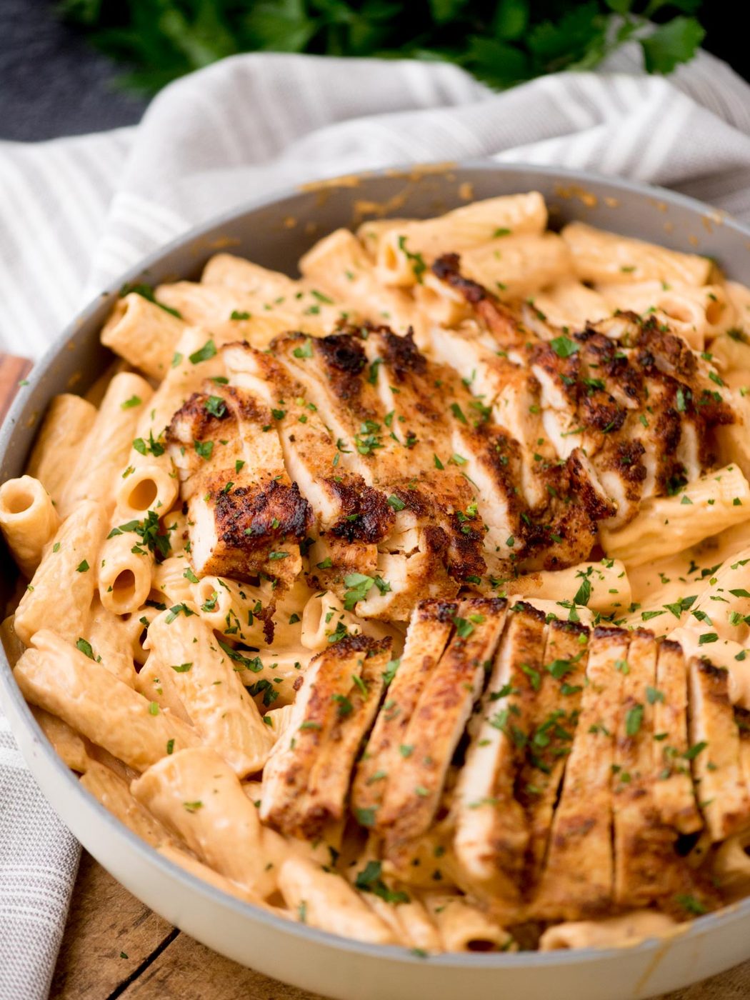 sliced chicken on top of pasta in a creamy cajun chicken pasta sauce in a skillet on top of a wooden board