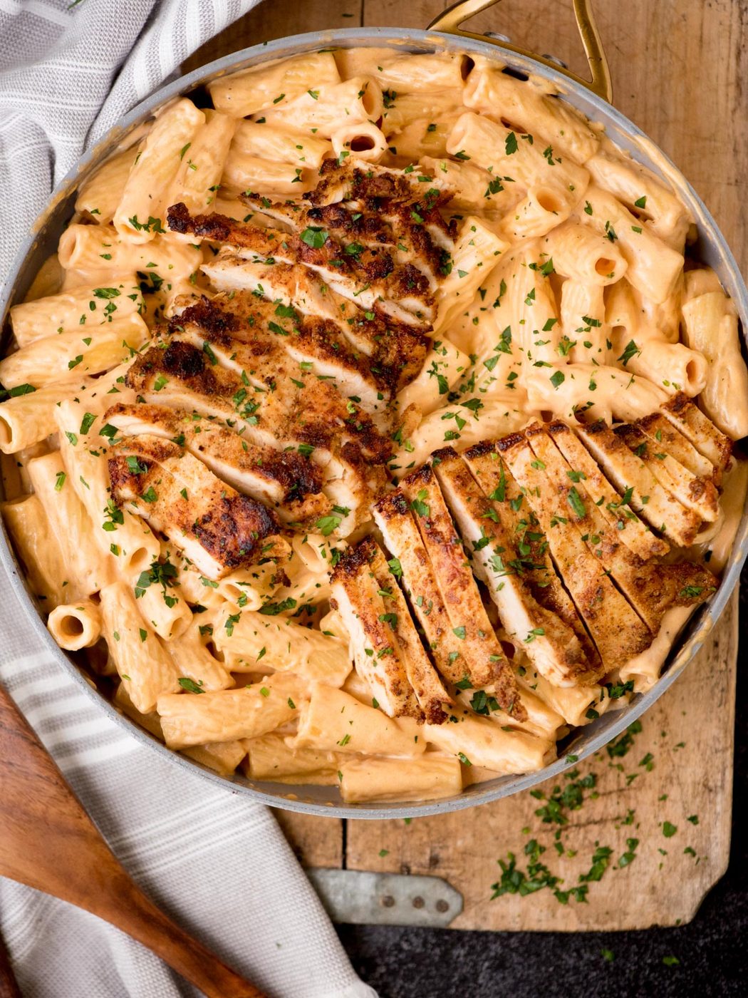 A skillet of Cajun chicken pasta featuring golden, sliced chicken breast served over rigatoni pasta coated in a creamy sauce, garnished with freshly chopped parsley.