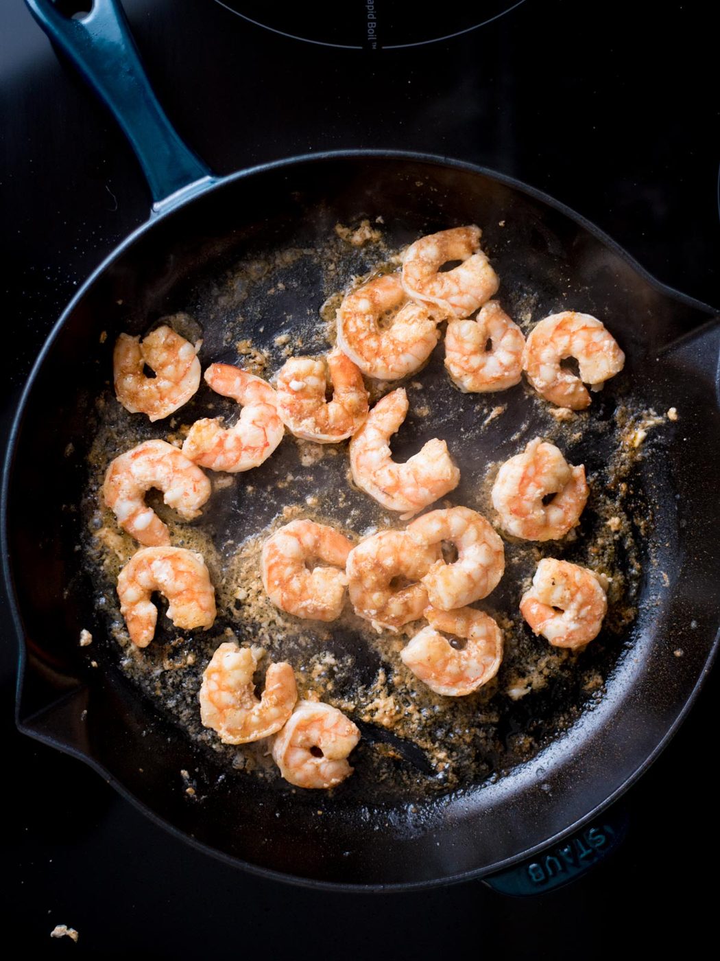 Shrimp cooking in a cast iron pan with avocado oil.