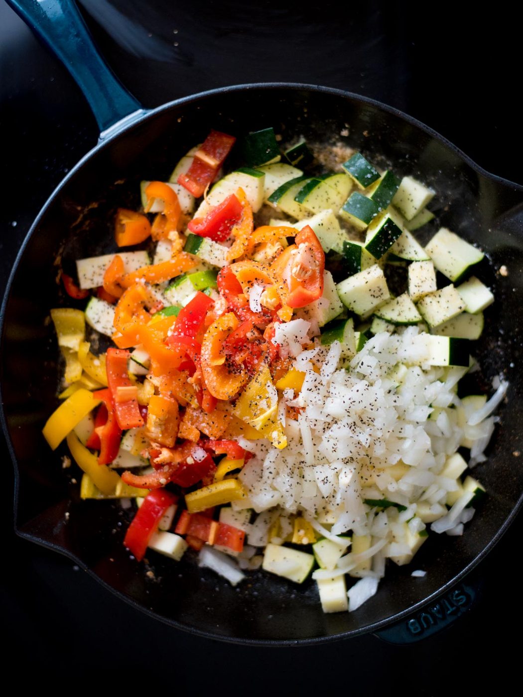 Diced veggies and seasonings added to a cast iron skillet.