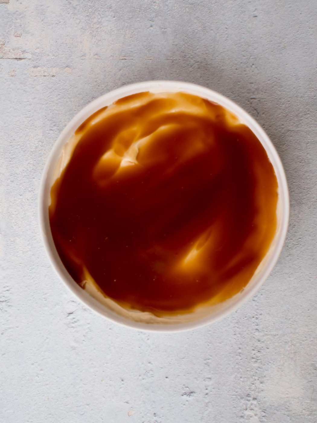 cream cheese layer topped with a caramel layer in a white dish of caramel apple dip