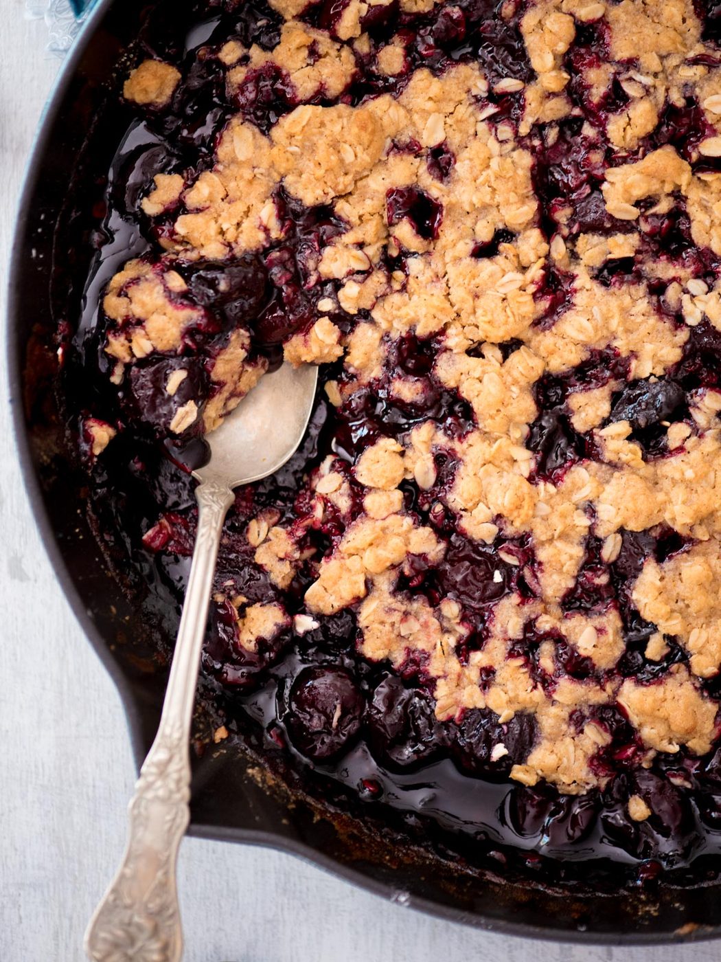 cherry crisp in a cast iron skillet being scooped with a spoon