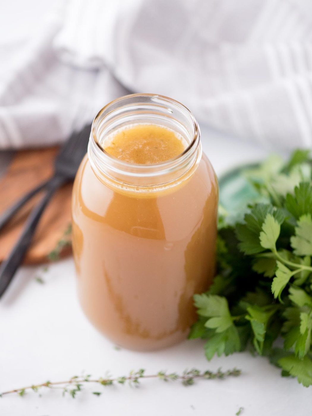 from-scratch chicken broth in a mason jar surrounded by fresh thyme and parsley