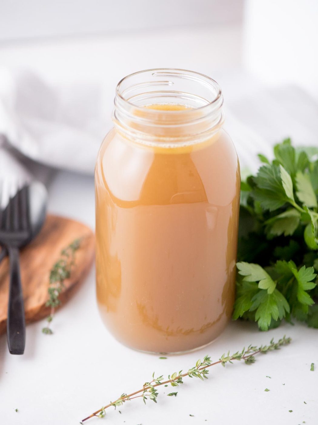 from-scratch chicken broth in a mason jar surrounded by fresh thyme and parsley