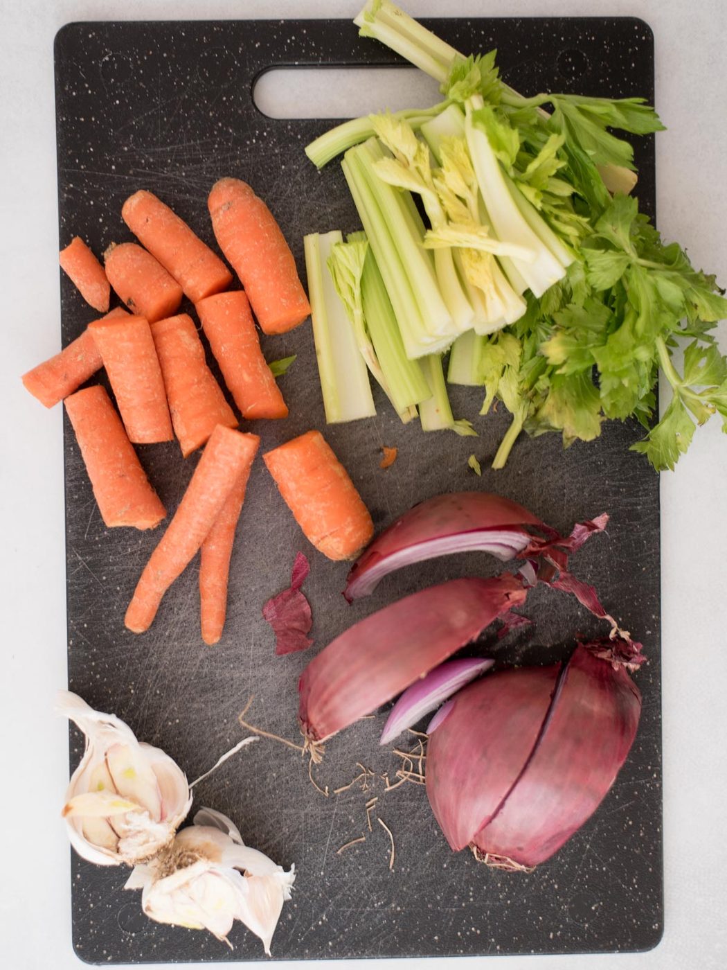 chopped celery, carrots, garlic, and onion on a cutting board