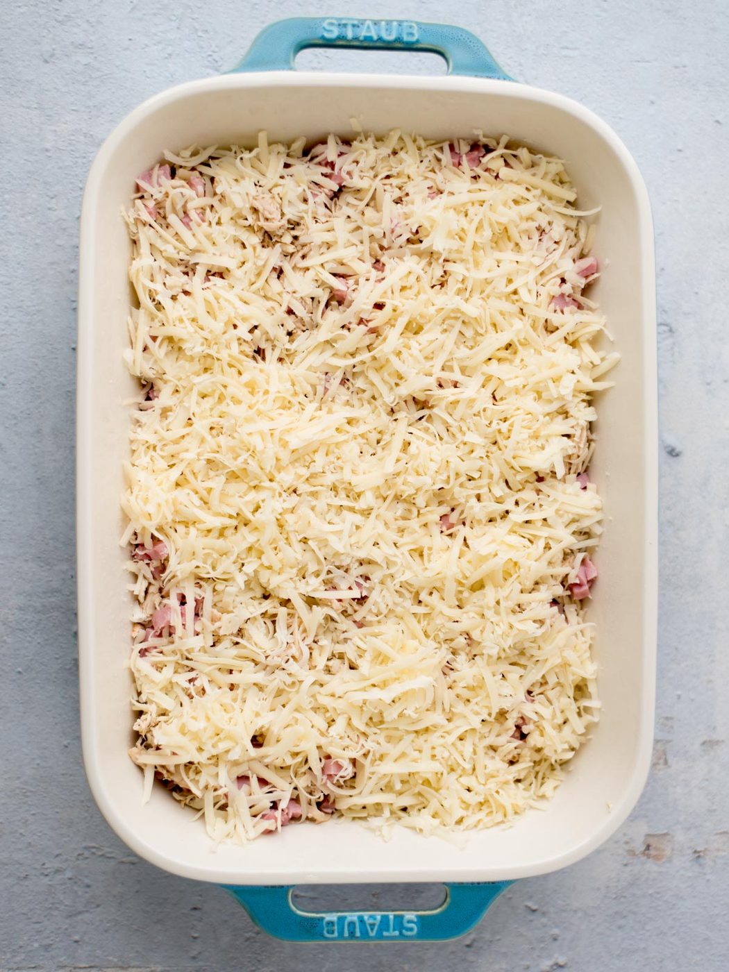 assembly of chicken cordon bleu casserole where the chicken, ham, and Swiss are in the baking dish