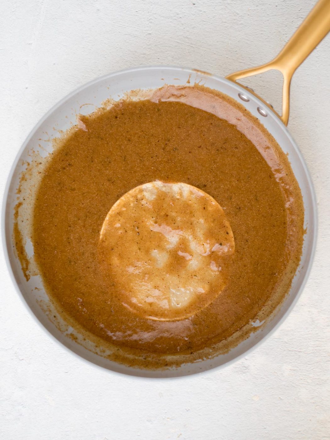 tortilla being coated in from-scratch enchilada sauce in a skillet