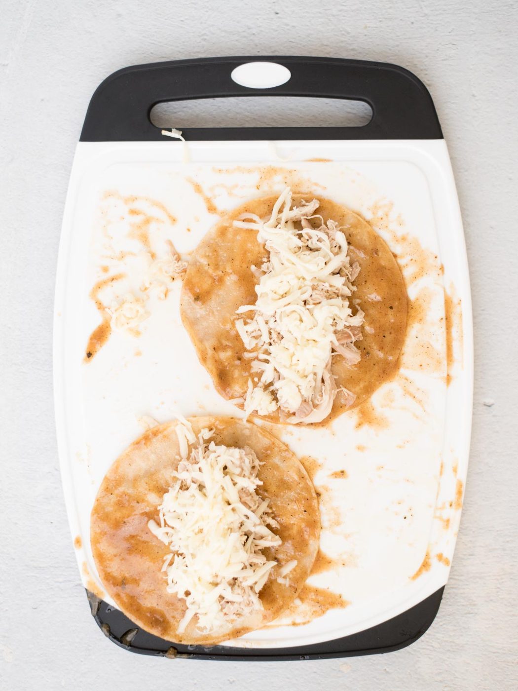 cheese and chicken on top of sauced tortillas on a cutting board