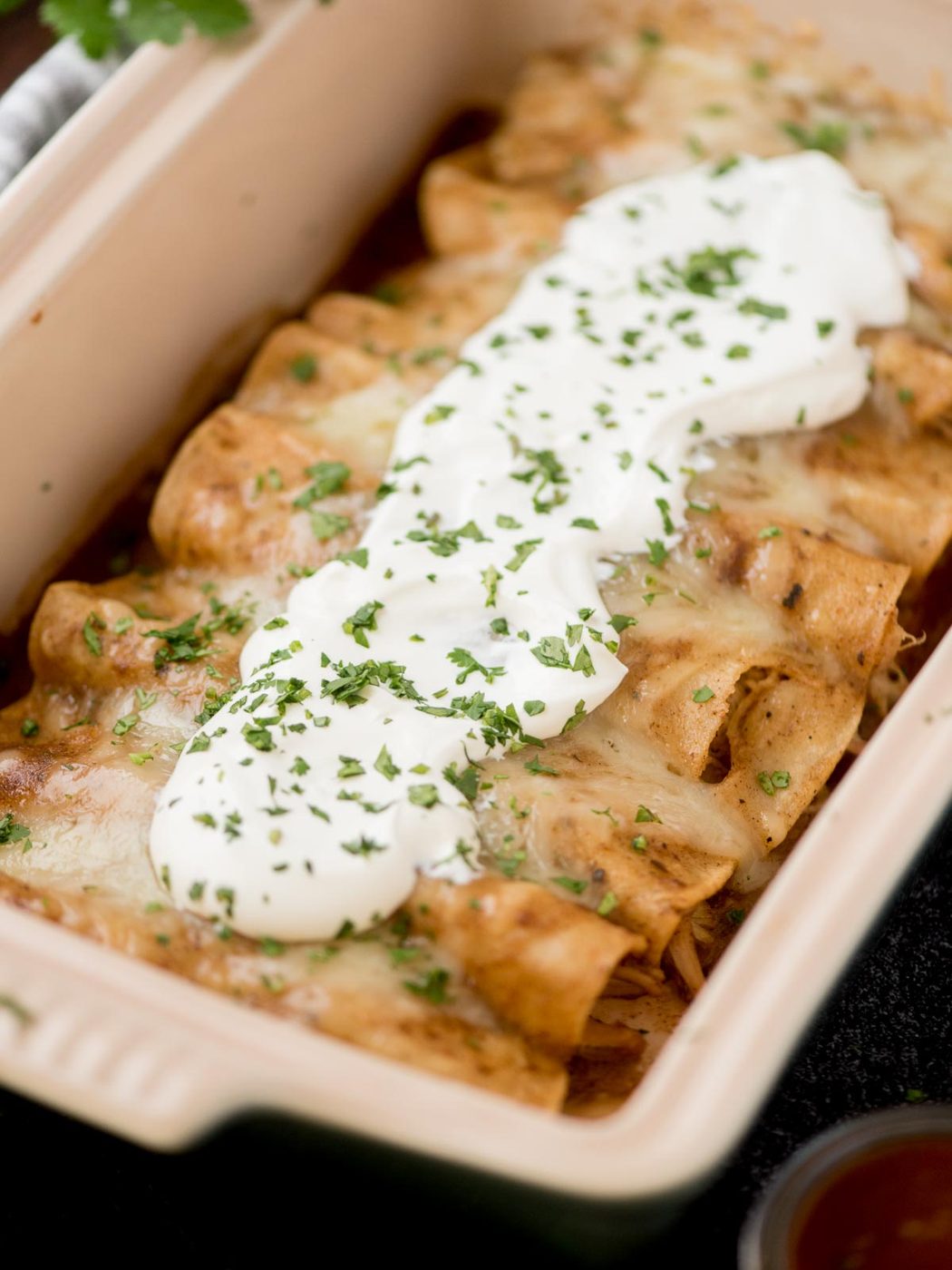 chicken enchiladas in a baking dish topped with sour cream and fresh cilantro