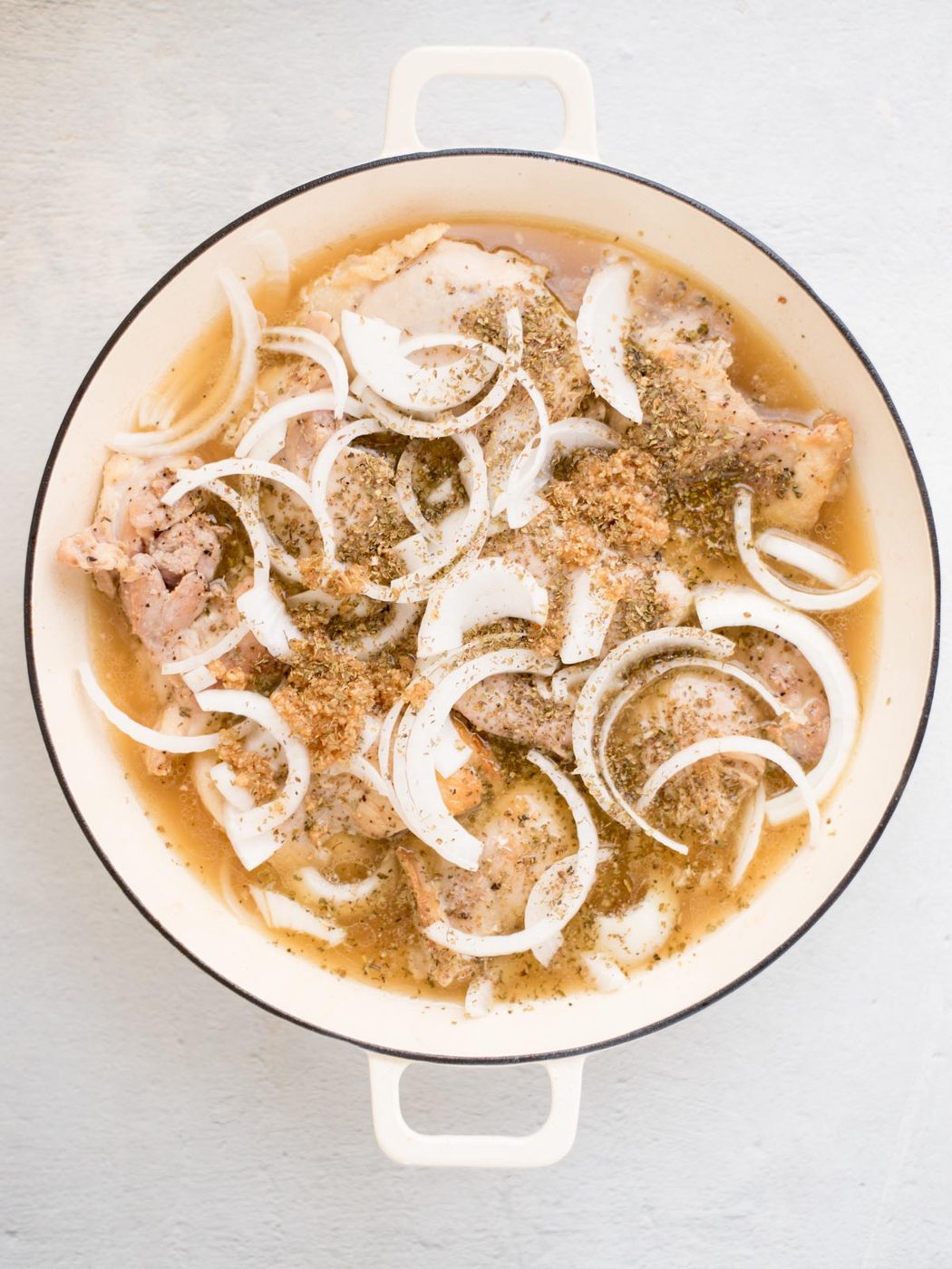 seared chicken, onions, spices, and broth in a pan