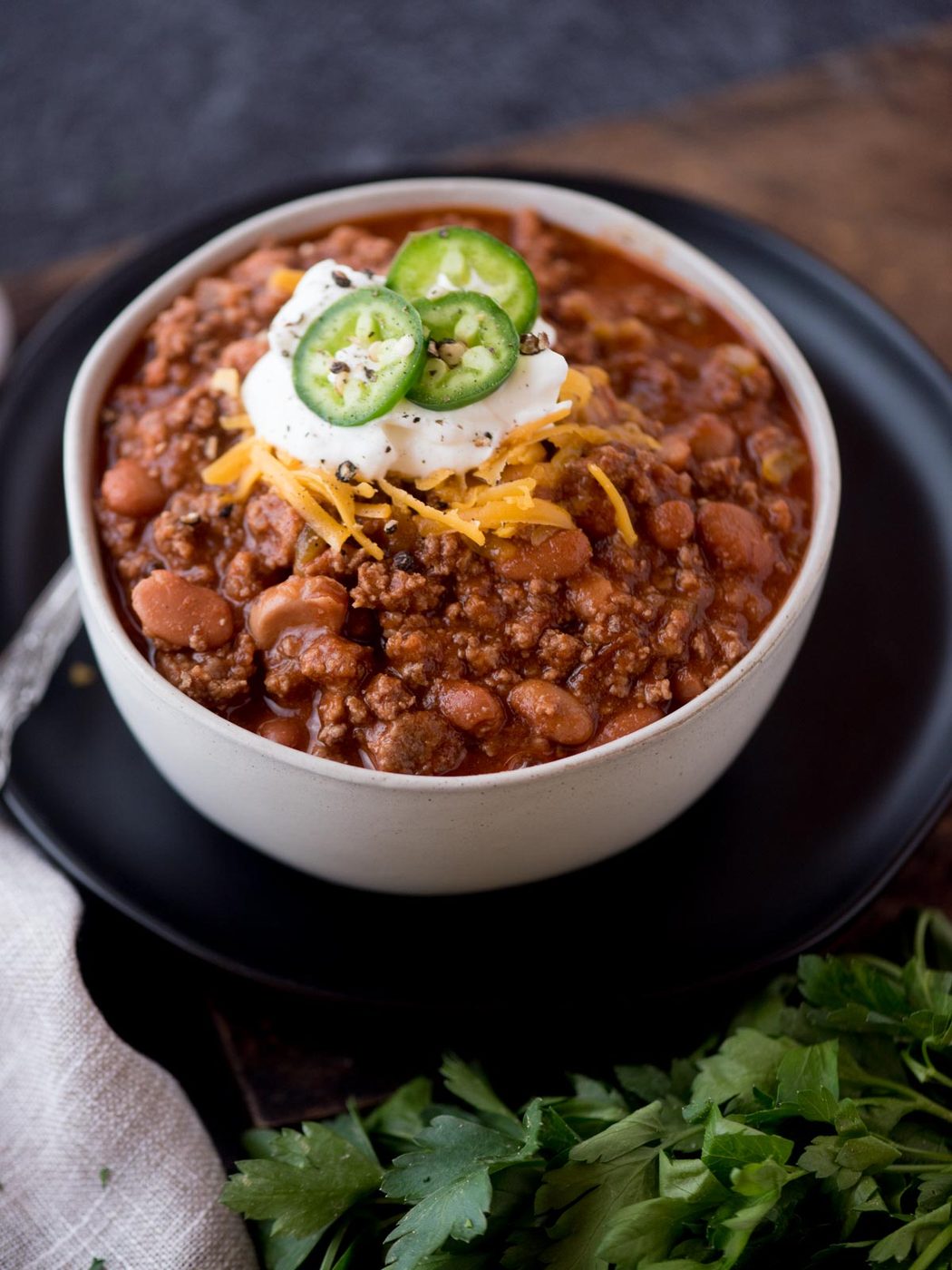 chili topped with cheese, sour cream, and jalapeno in a bowl surrounded by cilantro