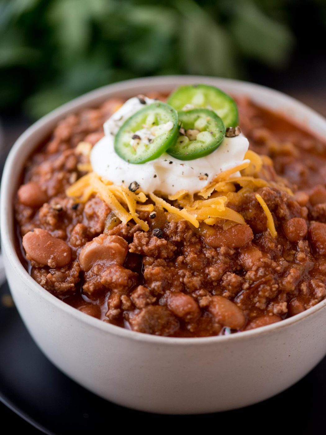 chili in a bowl topped with cheese, sour cream, and jalapeno