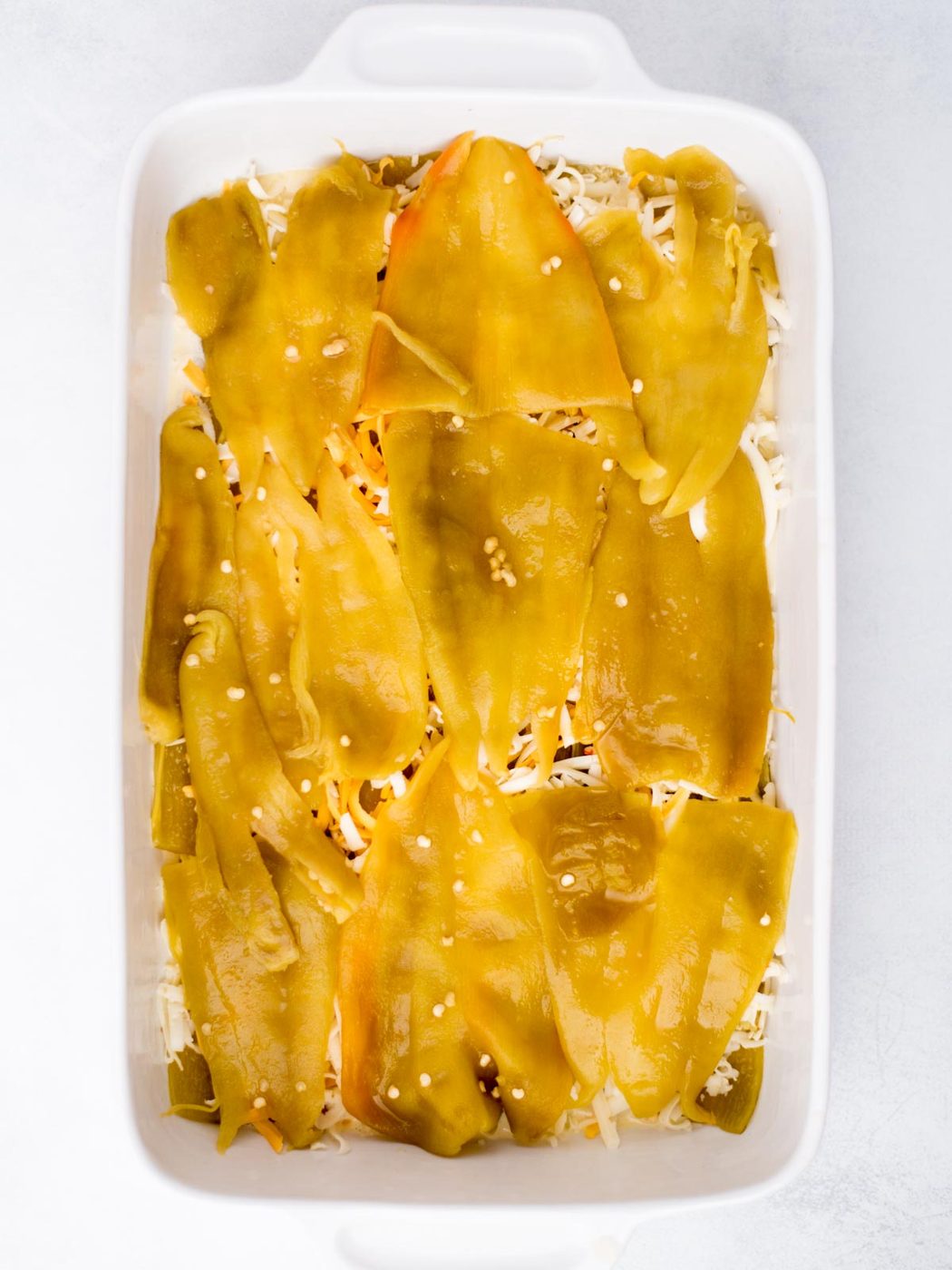 Second layer of hatch chiles added to the shredded cheese in the baking dish.