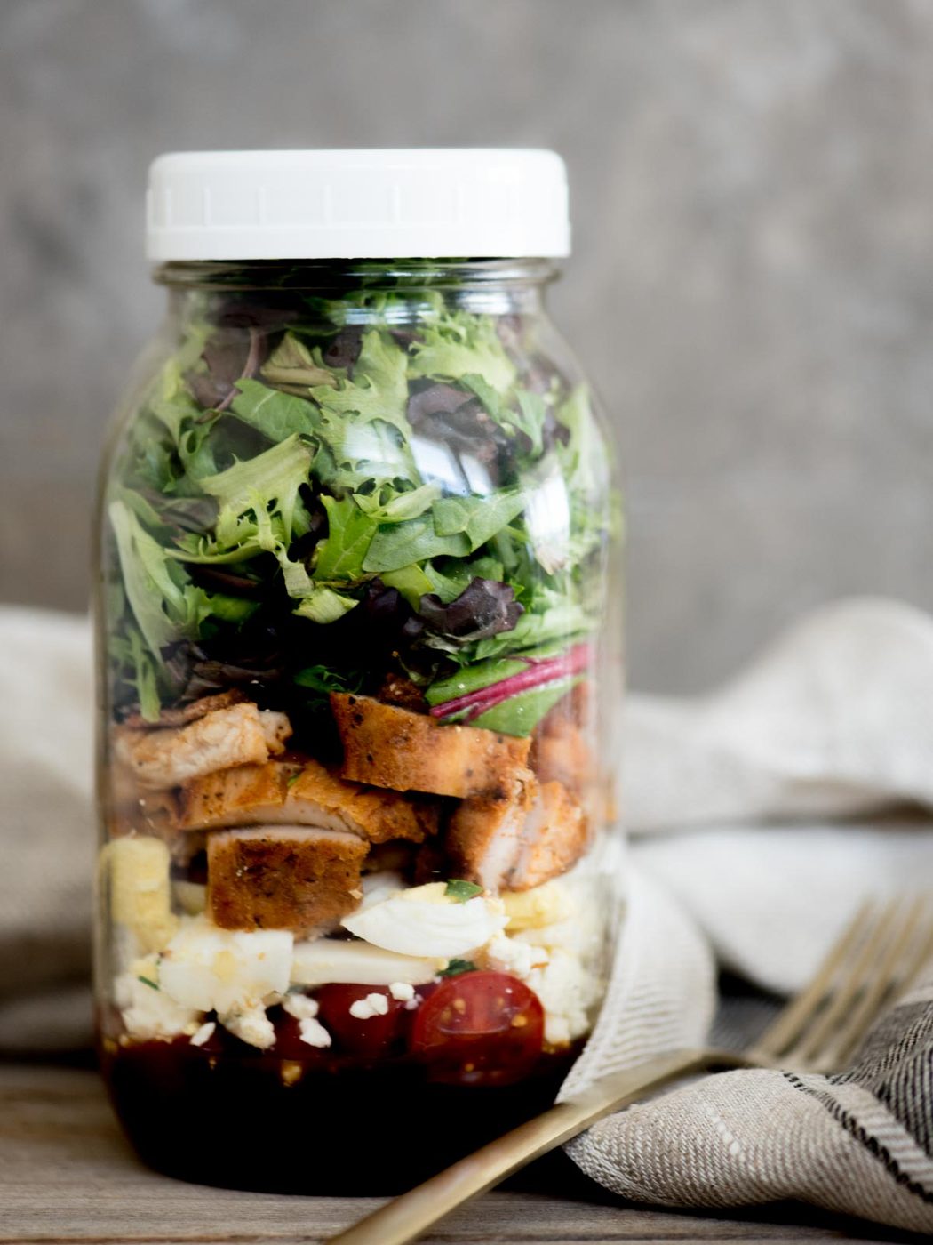 cobb style mason jar salad with lid on and a fork sitting next to it