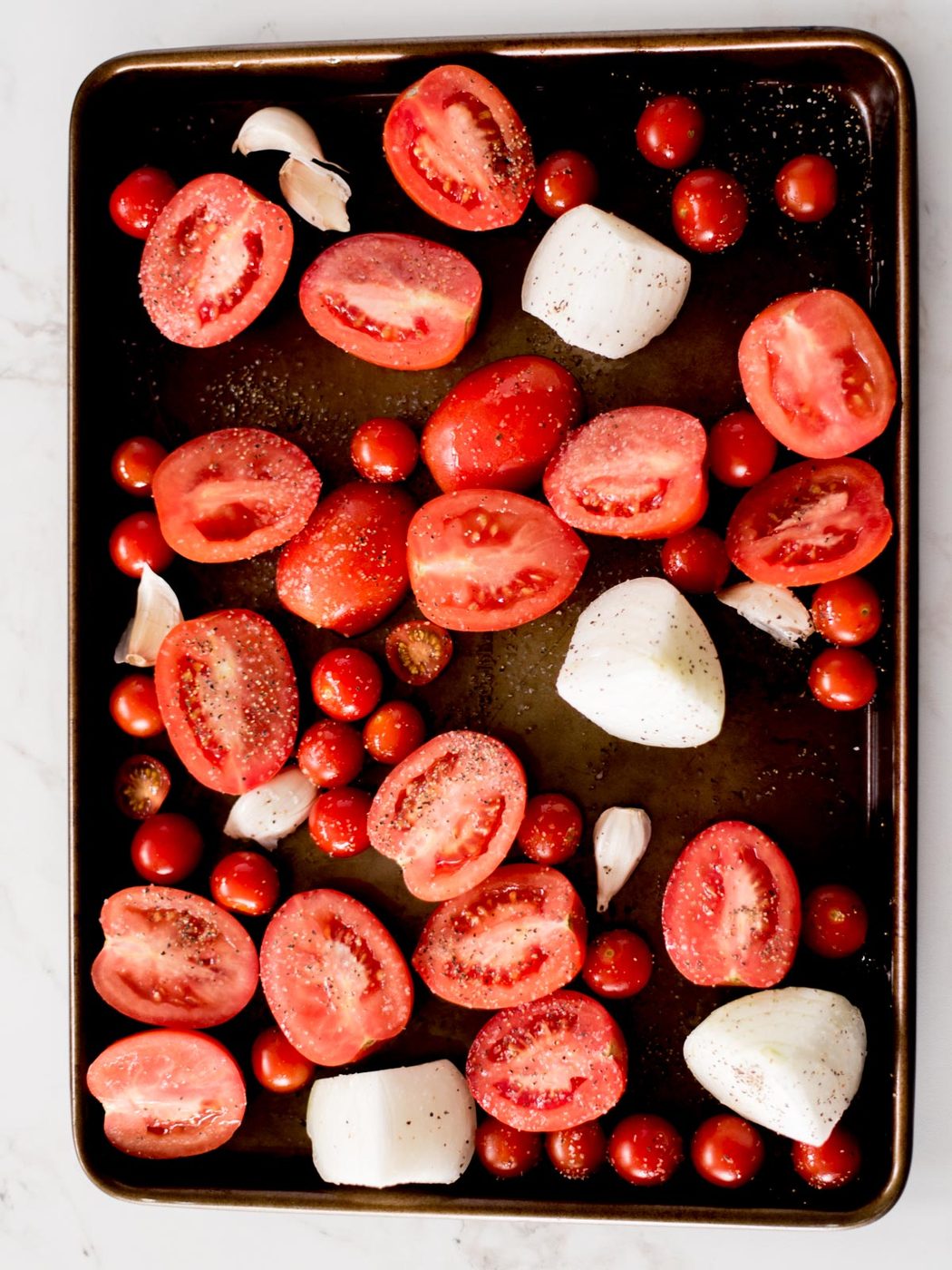 roma tomatoes, cherry tomatoes, garlic, and onion on a sheet pan sprinkled with olive oil, salt, and pepper
