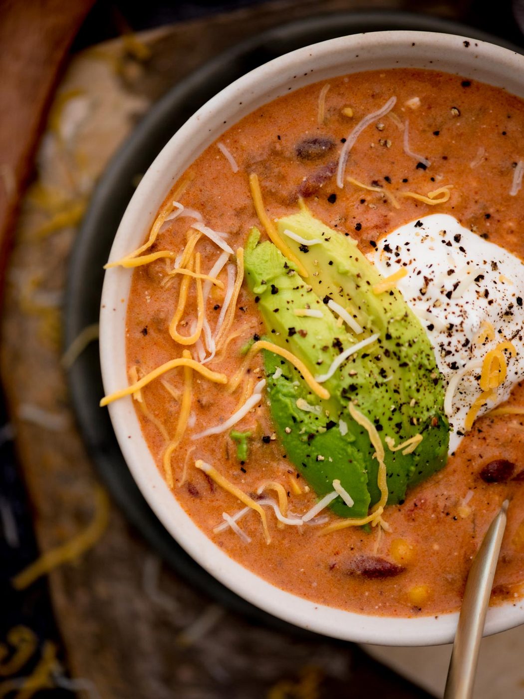 Partial view of a bowl of creamy taco soup with avocado and sour cream over the top.