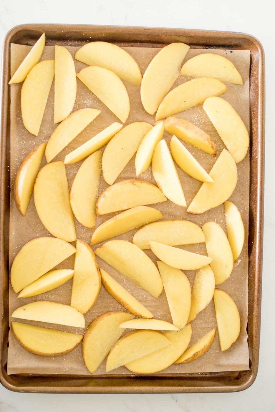 potato wedges on a parchment lined baking sheet seasoned with salt