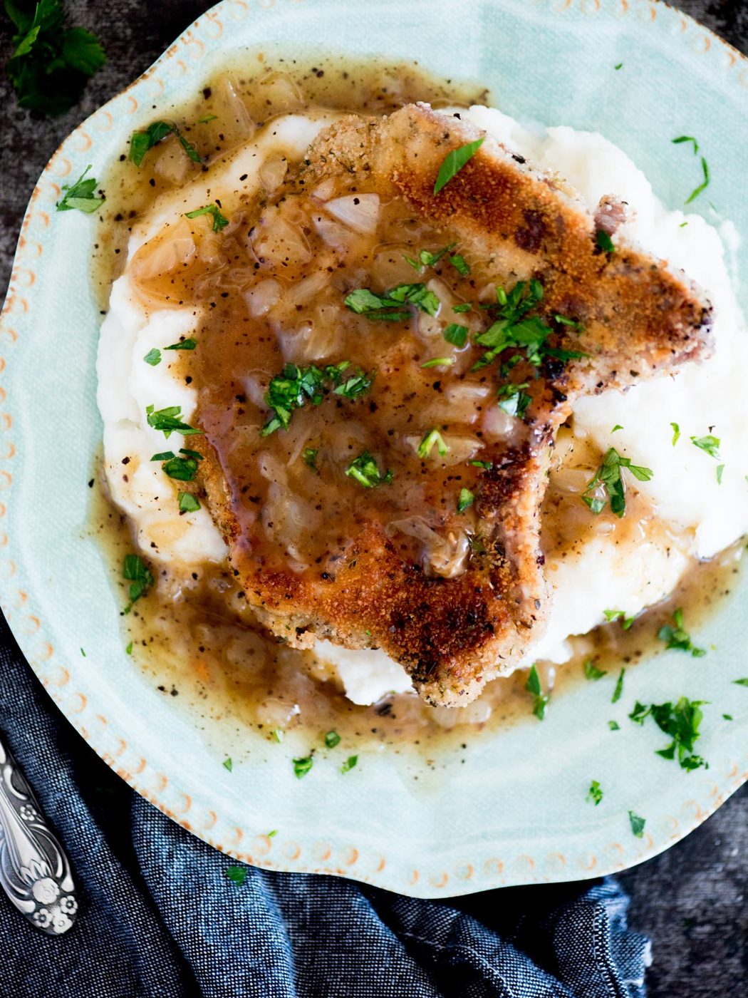 crispy fried pork chops with gravy over a bed of mashed potatoes on a plate