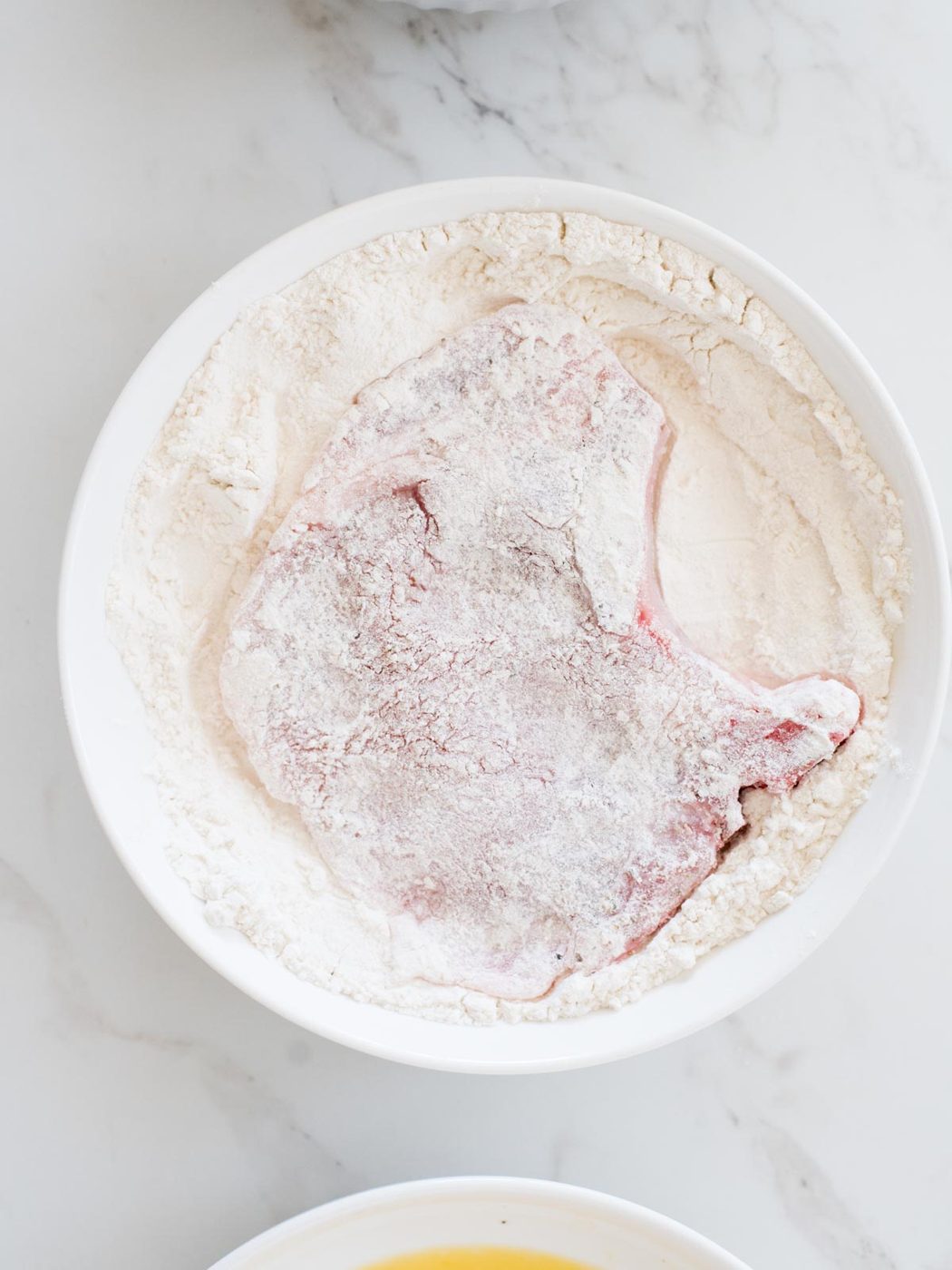 pork chop being dredged in flour