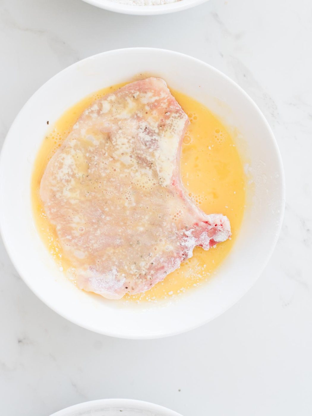 pork chop being dredged in eggs
