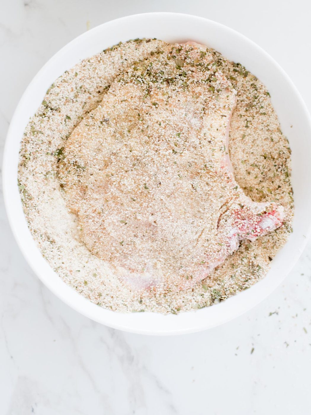 pork chop being dredged in breadcrumbs