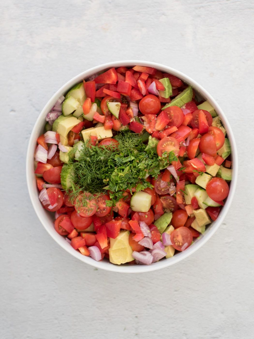 Chopped dill and parsley added to the chopped ingredients for cucumber tomato salad.