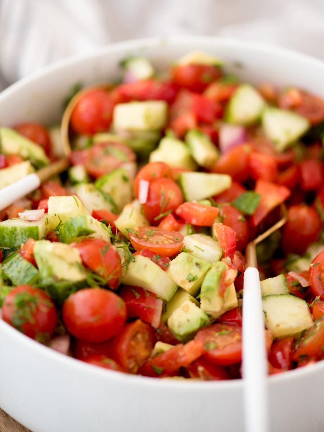 Large bowl of cucumber tomato salad with a serving spoon laying in it.