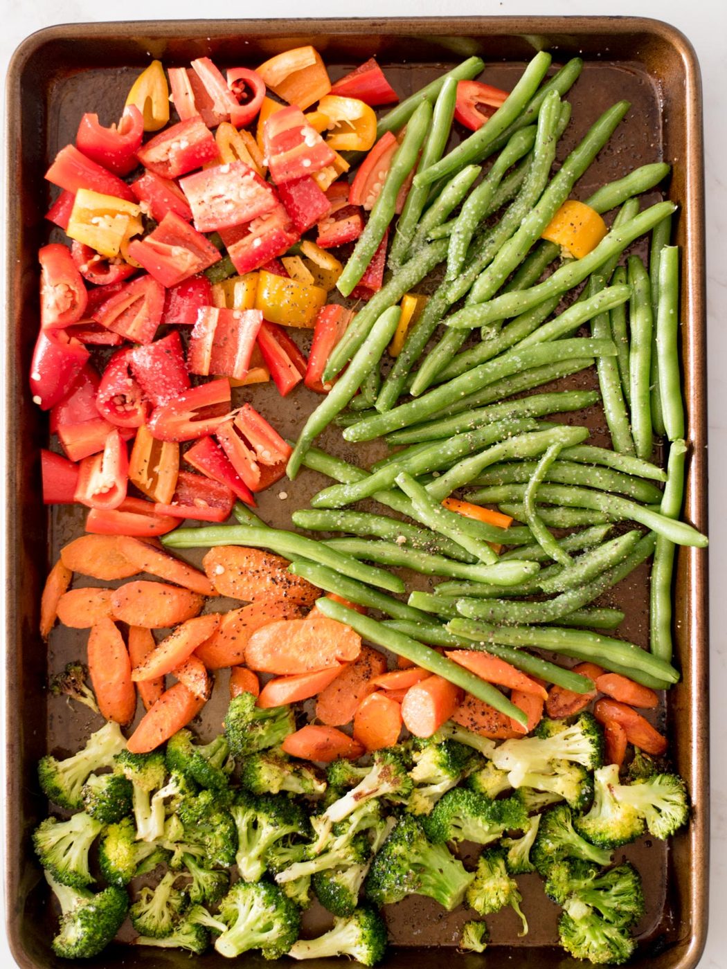 bell pepper, green beans, carrots, and broccoli on a sheet pan seasoned with salt and pepper