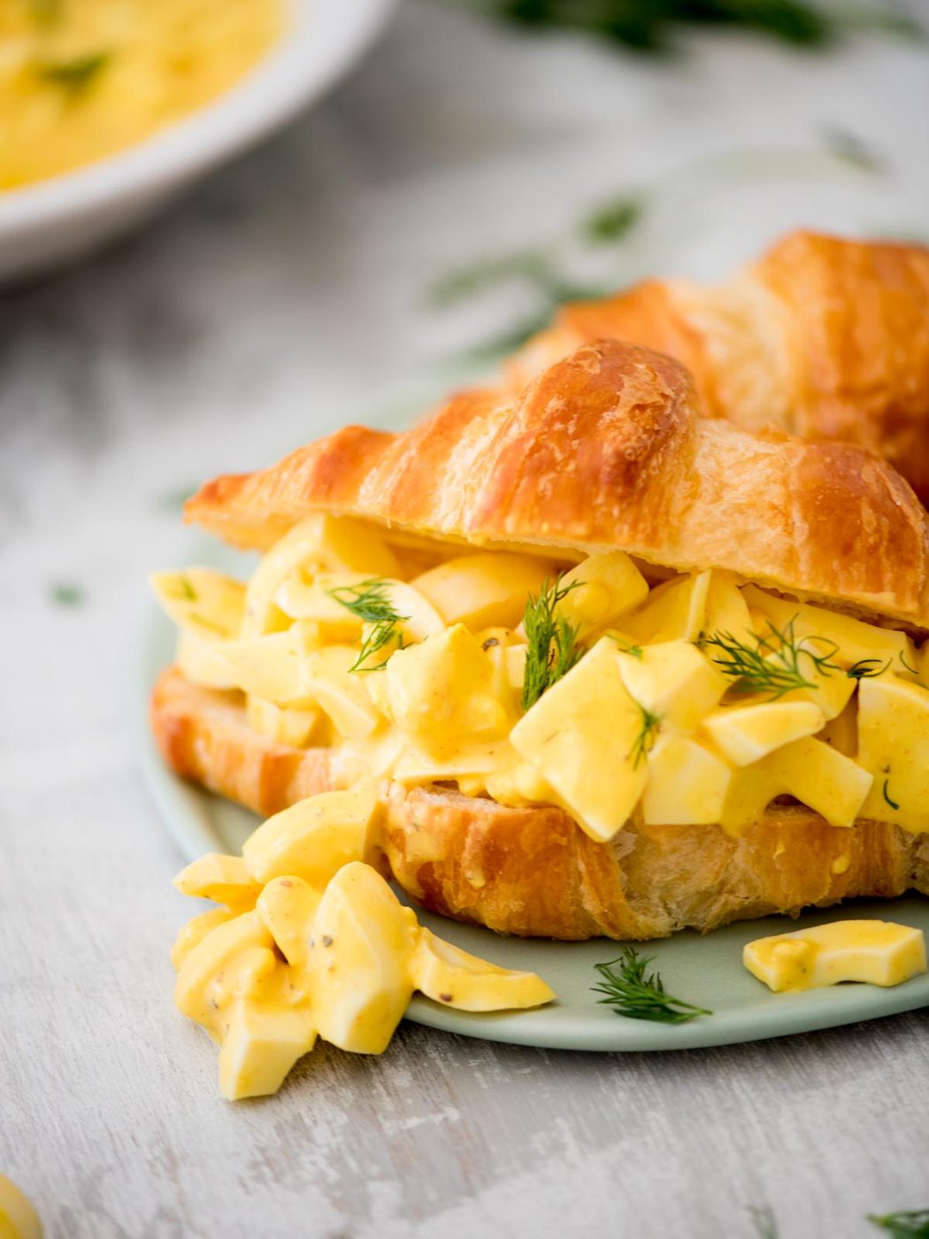 straightforward egg salad on a croissant topped with fresh dill