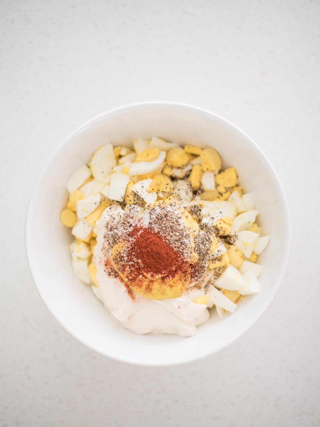 salt, pepper, and paprika added to the egg salad recipe ingredients in a mixing bowl