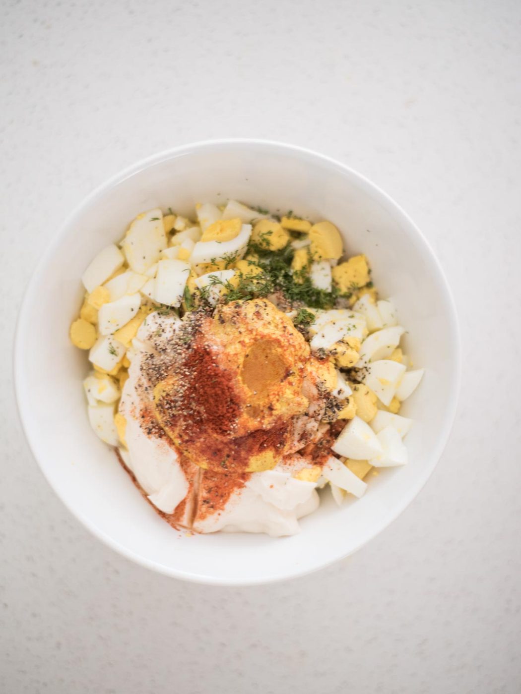 pickle juice added into the egg salad recipe ingredients in a mixing bowl