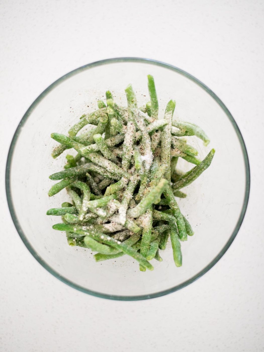 top view of frozen green beans in a mixing bowl with seasonings sprinkled on top.