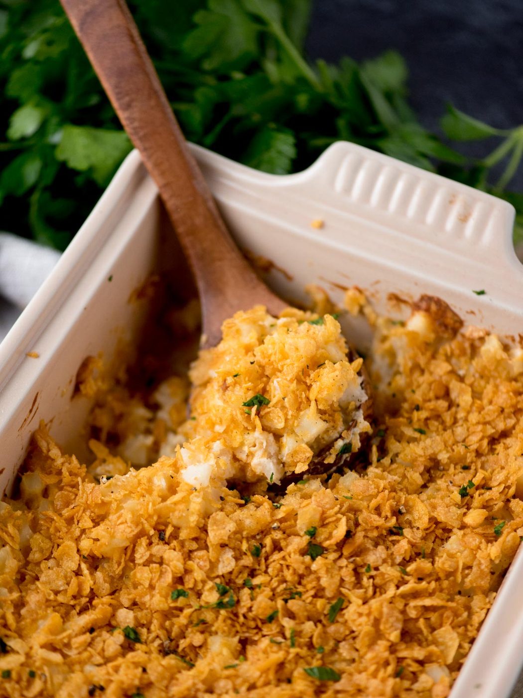 baking dish with funeral potatoes being scooped out with a wooden spoon