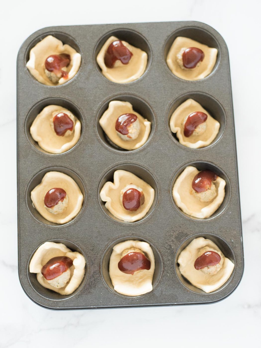 bbq sauce on meatballs in crescent dough in a muffin tin