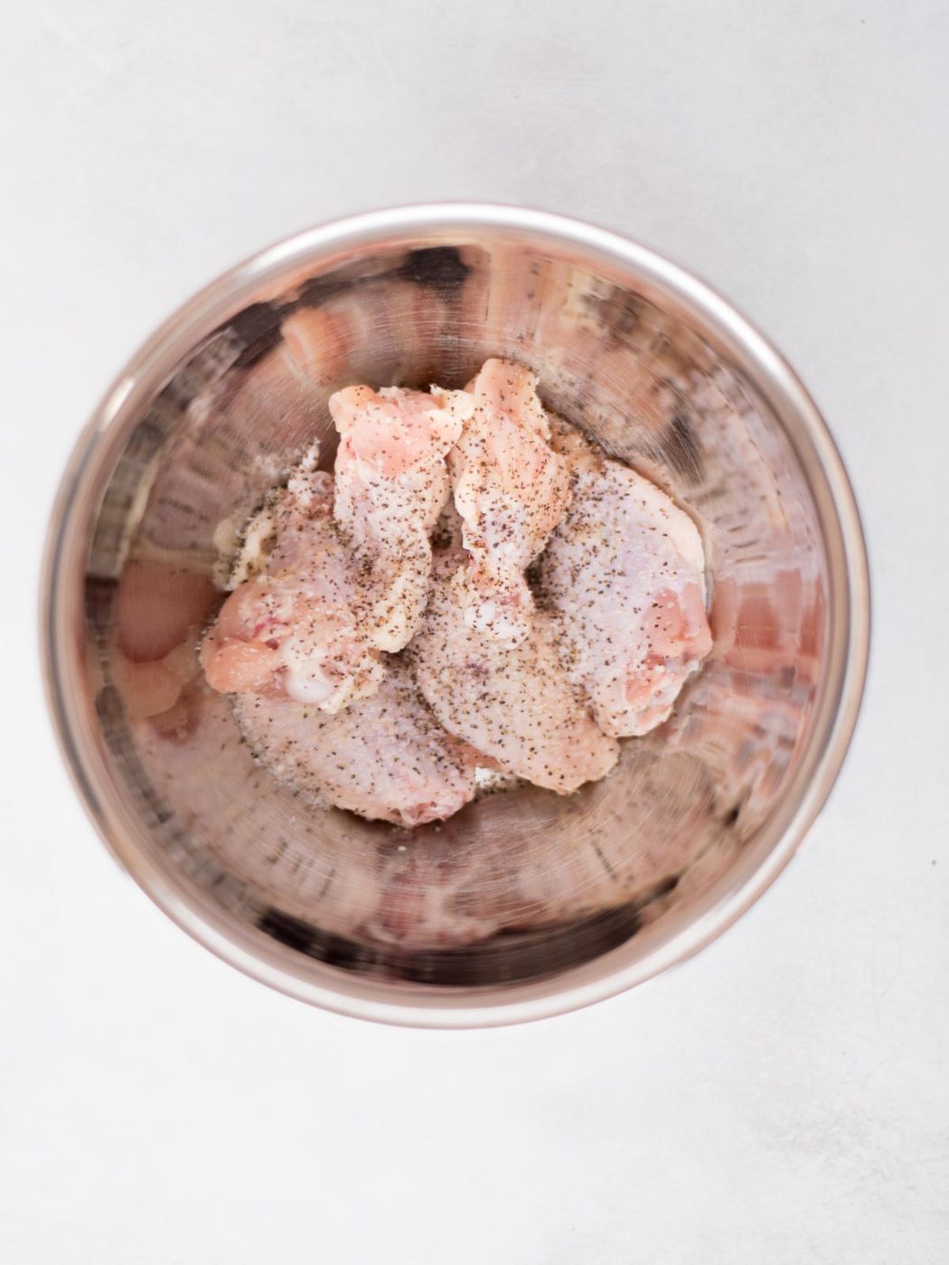 raw wings sprinkled with seasoning in a mixing bowl