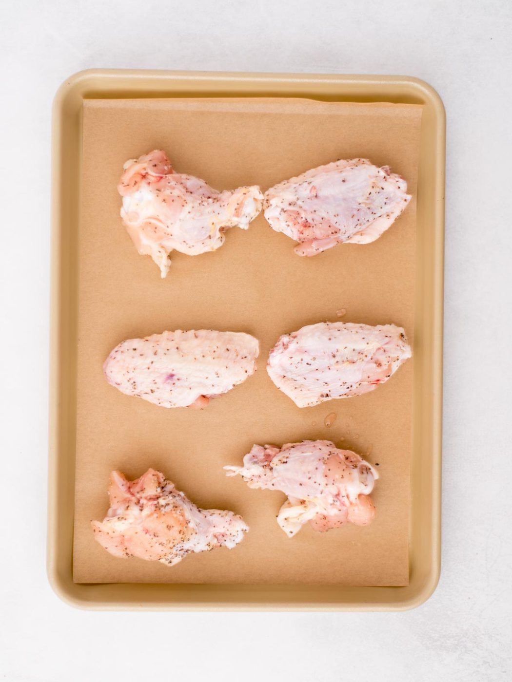 raw seasoned wings on a parchment lined baking sheet