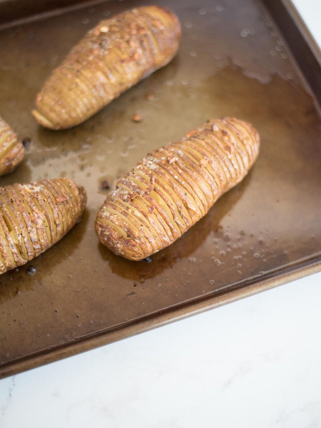 hasselback potato cooked halfway through on a baking sheet