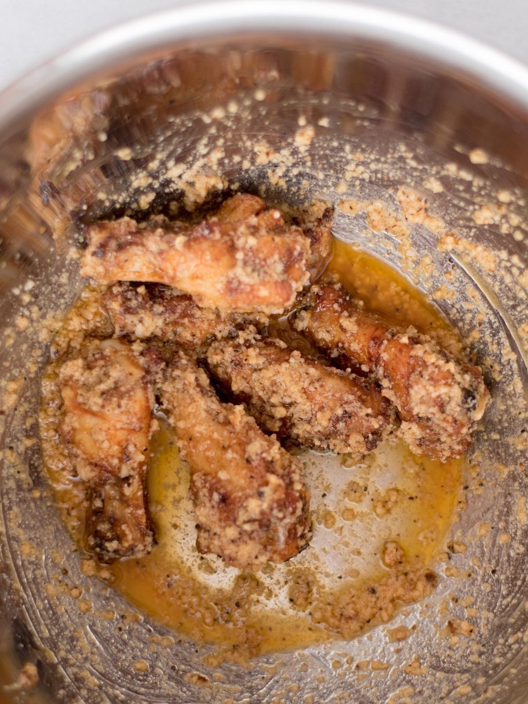 garlic parmesan sauce mixed with cooked wings in a mixing bowl