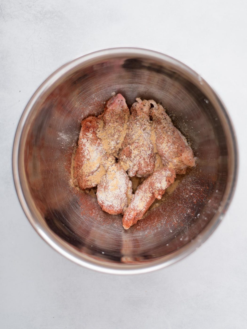 wings in a bowl seasoned with salt, pepper, garlic powder, onion powder, and paprika