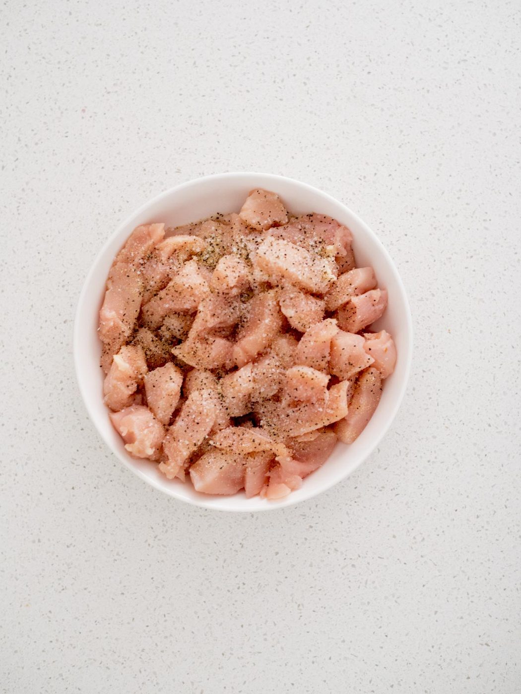 Seasoning sprinkled over raw chicken chunks in a bowl.