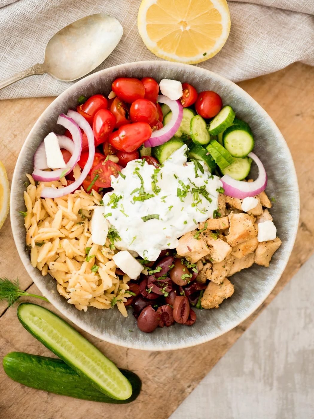 greek chicken bowl topped with tzatziki surrounded by cucumbers and dill