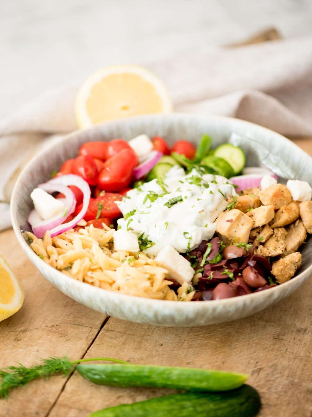 greek chicken bowl surrounded by cucumbers and dill