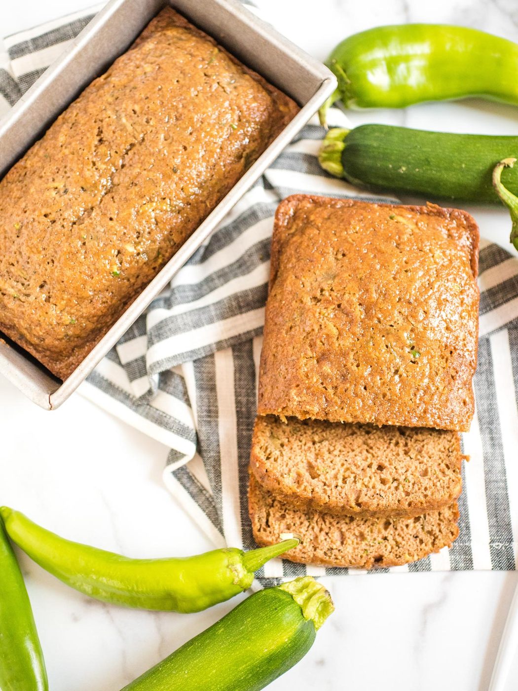 sliced loaf of green chile zucchini bread on a striped cloth next to second loaf