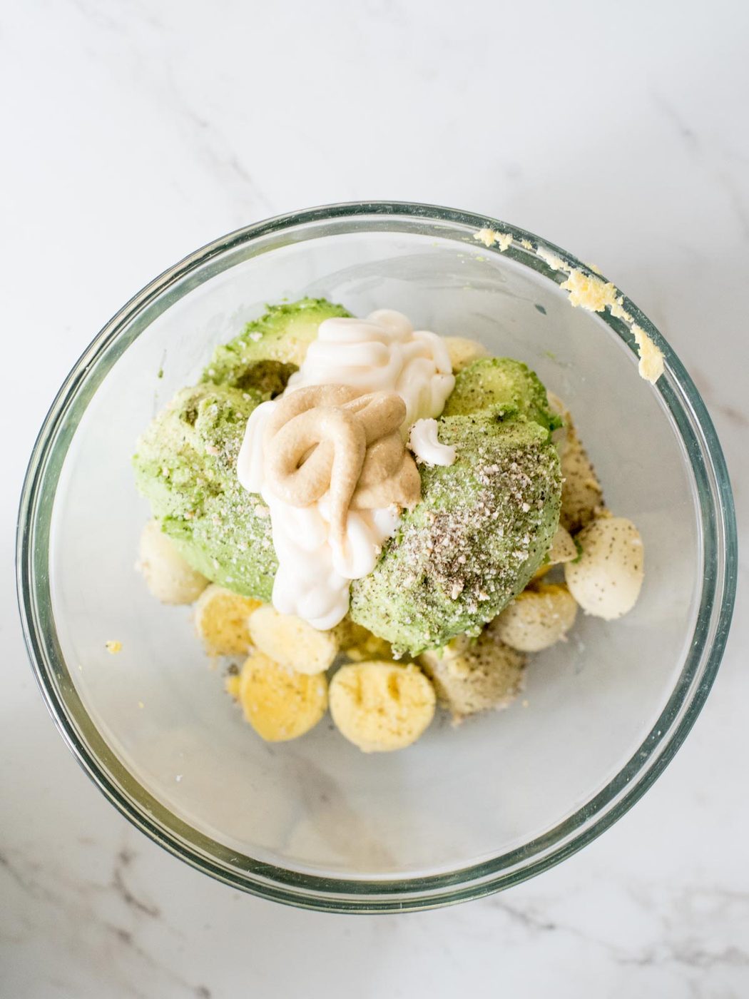 dijon mustard added to mixing bowl with avocado, mayo, seasonings, and yolks