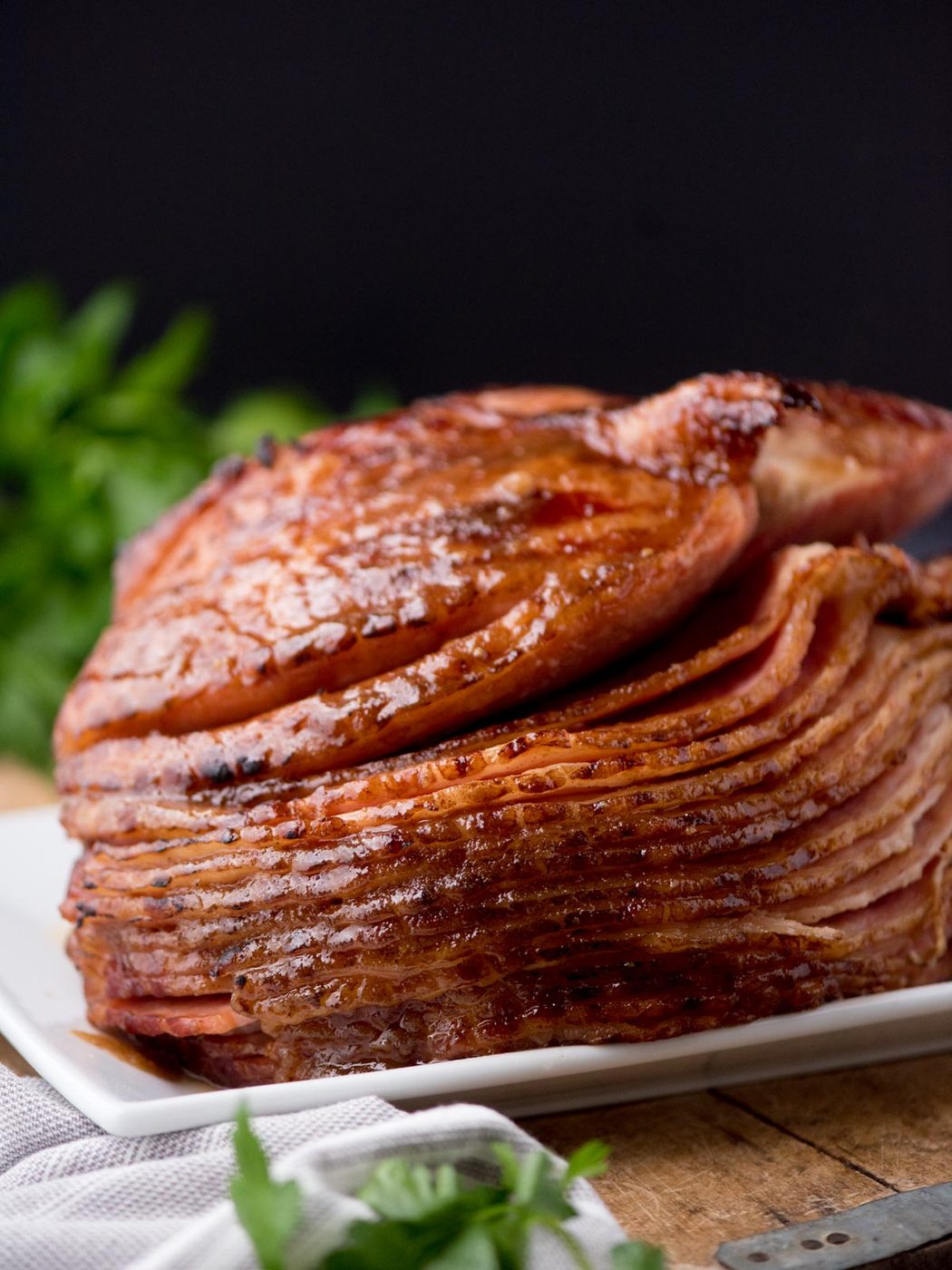 brown sugar glazed ham on a plate surrounded by a kitchen towel and parsley