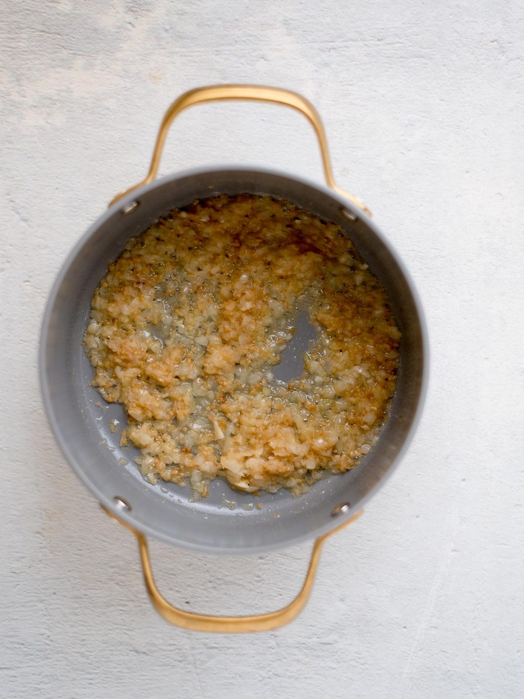 A saucepan with golden, sautéed onions and garlic, cooking in melted butter. The onions are translucent and beginning to brown, indicating they are well-cooked