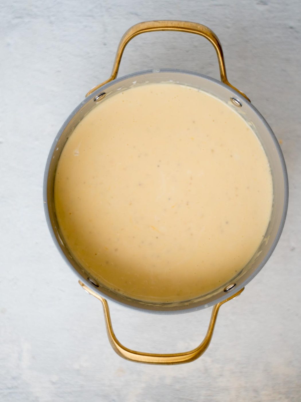 A saucepan filled with a creamy cheese sauce, smooth and pale yellow in color, ready to be mixed with hash browns for the casserole."