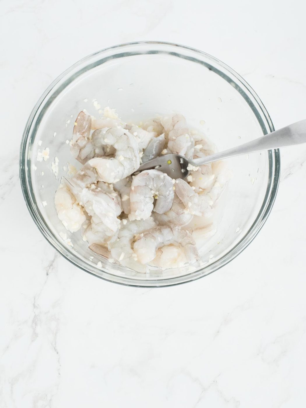 raw shrimp tossed with minced garlic and white wine in a mixing bowl for baked shrimp scampi