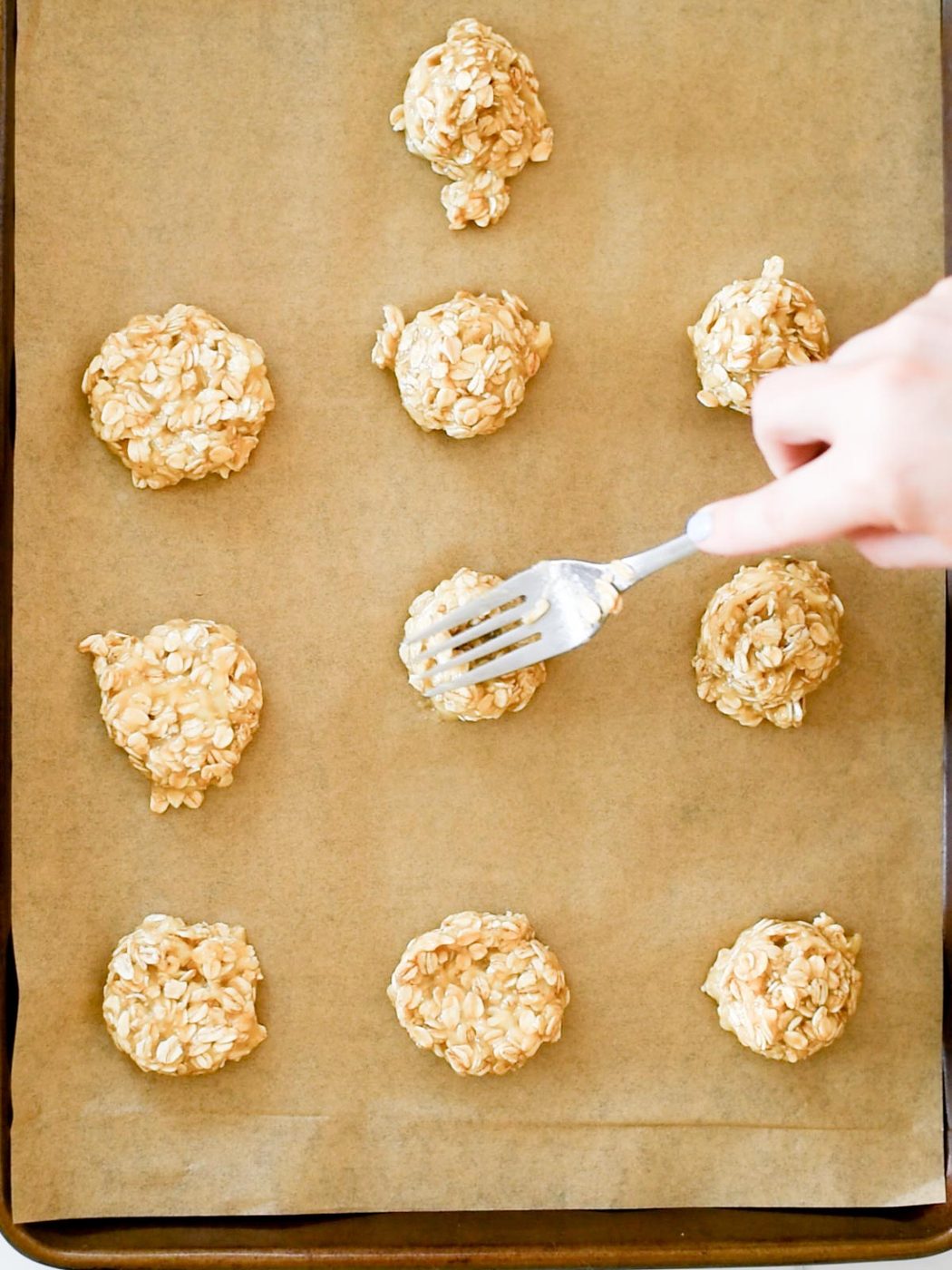 cookie dough being gently pushed down with a fork on a parchment lined baking sheet